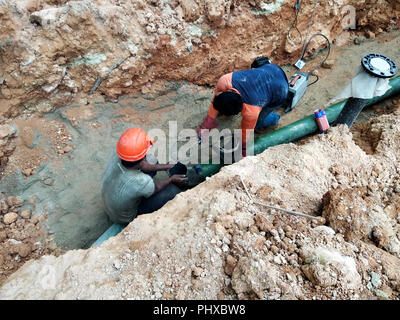 Utilità della metropolitana e tubazione di servizi prevista dai lavoratori nelle trincee presso il cantiere. Installazione del giunto tubo e il raccordo a gomito in corso. Foto Stock