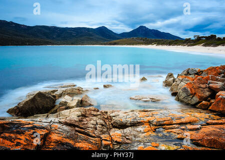 Il giorno di esposizione lungo la cattura della Wineglass Bay nel Parco Nazionale di Freycinet, Tasmania, Australia, con lichene arancione su rocce di granito in primo piano. Foto Stock