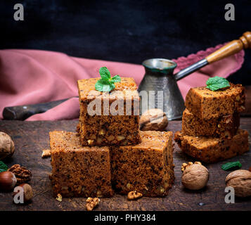 Pila di piazza al forno fette di torta con le noci su un marrone tavola di legno, un pan di spagna, close up Foto Stock