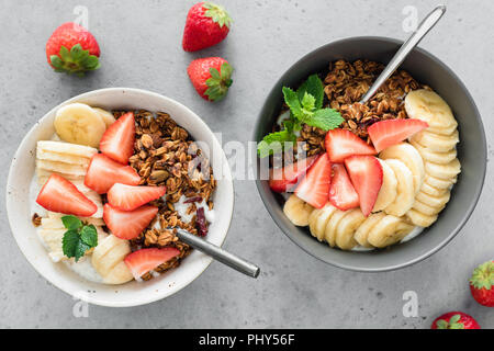 Sana colazione ciotola di muesli, yogurt e frutta. Fragola, banana e crunchy granola con yogurt in un recipiente su sfondo di calcestruzzo. Vista superiore Foto Stock