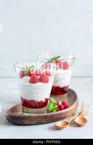 Budino di Chia con lamponi in un vetro su legno scheda servente. Copia spazio per il testo. Concetto di stile di vita sano, mangiare sano, vegane e vegetar Foto Stock