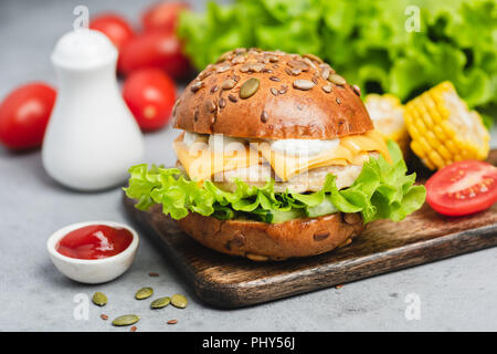 Pollo cheeseburger in legno che serve di bordo su sfondo di calcestruzzo. Primo piano Foto Stock