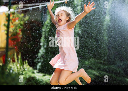 Un allegro incantevole bambina di sette anni gode di una posizione soleggiata mattinata estiva e si diverte nel giardino di casa. Foto Stock