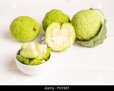 Frutta verde di maclura pomifera,osage orange,cavallo apple,adam Apple a crescere su bianco tavolo in legno. Maclura pezzi nella piastra pronta per la preparazione di unguento. Maclura uso nella medicina alternativa. Spazio di copia Foto Stock