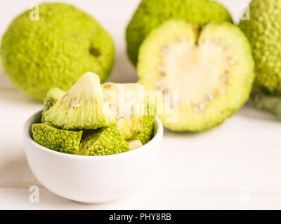 Frutta verde di maclura pomifera,osage orange,cavallo apple,adam Apple a crescere su bianco tavolo in legno. Maclura pezzi nella piastra pronta per la preparazione di unguento. Maclura uso nella medicina alternativa. Spazio di copia Foto Stock