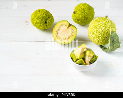 Frutta verde di maclura pomifera,osage orange,cavallo apple,adam Apple a crescere su bianco tavolo in legno. Maclura pezzi nella piastra pronta per la preparazione di unguento. Maclura uso nella medicina alternativa. Spazio di copia Foto Stock