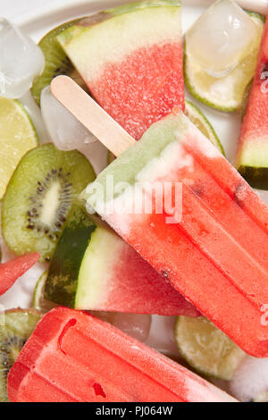 Close-up di anguria gelato per lecca-lecca . Piastra bianca con fette di frutta e cubetti di ghiaccio e gelato biologico . Sana dessert estivo. Lay piatto Foto Stock