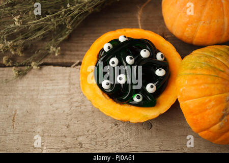 Spooky Halloween party food - gummy jelly worms in zucca con occhi monsret su sfondo di legno, festa close up Foto Stock