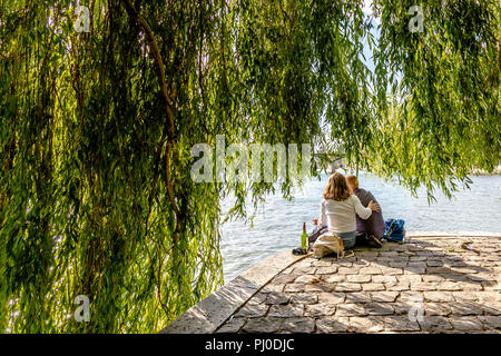 L uomo e la donna seduta vicino a ogni altro sul bordo del fiume Senna da Square du Vert-Galant a Parigi, con una bottiglia di vino accanto a loro. Foto Stock