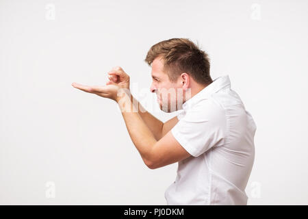 Positivo uomo bello mostra qualcosa di molto piccolo o piccola, essendo in dubbio l'umore, pone contro whitebackground. Foto Stock