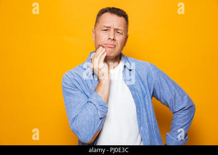 Ritratto di un fastidio uomo di mezza età che soffre di un mal di denti isolate su sfondo giallo Foto Stock