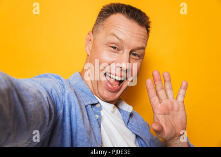 Ritratto di un allegro uomo di mezza età tenendo un selfie con mano distesa isolate su sfondo giallo Foto Stock