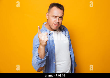 Ritratto di un arrabbiato uomo di mezza età puntare il dito isolate su sfondo giallo Foto Stock