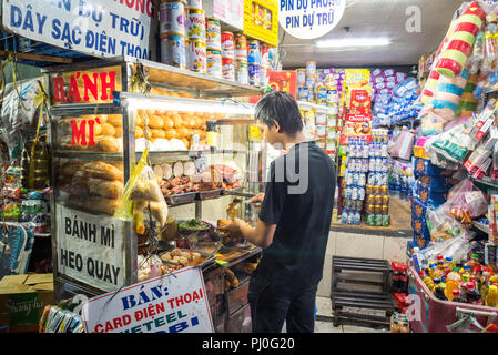 La città di Ho Chi Minh, Vietnam - 1 Maggio 2018: giovane cuochi banh mi usando gli ingredienti (Pane & tipi di carne) da una street food cart in strada di notte. Foto Stock