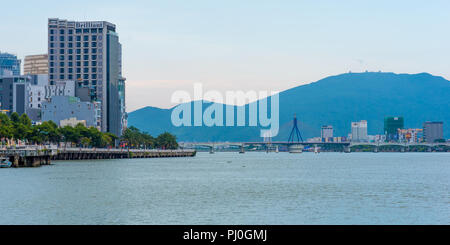 Da Nang, Vietnam - 6 Maggio 2018: Il fiume Han, Song Han ponte con montagne, il terrapieno (Bach Dang Street) & 4-stella brillante hotel in serata. Foto Stock