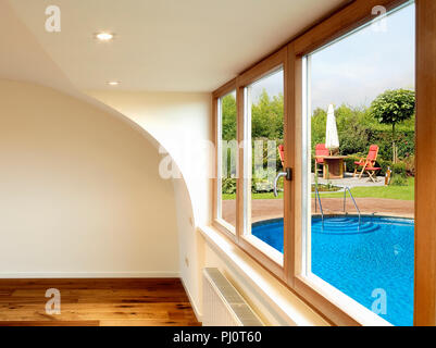 Arredamento moderno con pavimento in legno e un tavolo da pranzo con sedie, ombrellone in un lussureggiante giardino esterno Foto Stock
