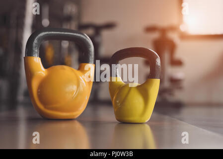 Due kettlebells colorati su una palestra per il fitness piano. Peso pesanti attrezzature sportive e accessori in allenamenti training club. Body building e muscolari stren Foto Stock