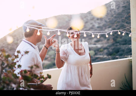 Felice caucasian persone che ballano insieme a casa in terrazza con luci durante il tramonto. romantico e il rapporto di concetto di immagine per le persone felici in Foto Stock