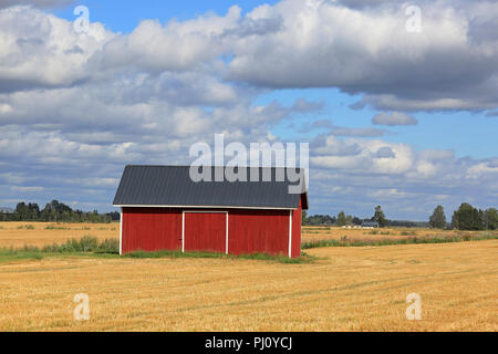 Rosso fienile in legno della stoppia campo di grano in autunno con il cielo blu e nuvole background nell aprire il paesaggio agricolo di Pohjanmaa, Finlandia Foto Stock