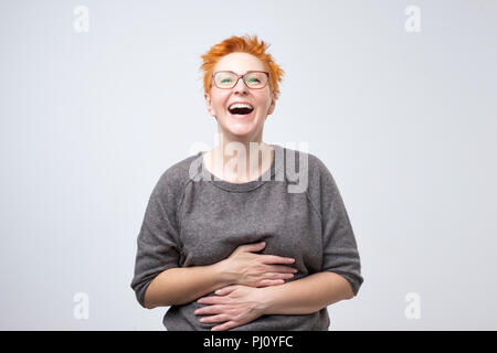 Close up ritratto di una bella metà donna adulta con capelli rossi ridere in piedi su sfondo grigio. Foto Stock