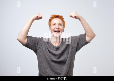 Allegra donna matura sorridente con pugni in rilievo che mostra la sua forza e la sua atmosfera positiva. Foto Stock