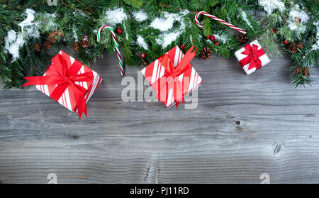 Coperta di neve albero di Natale evergreen rami con doni posto sulla sommità di un rustico sfondo di legno Foto Stock