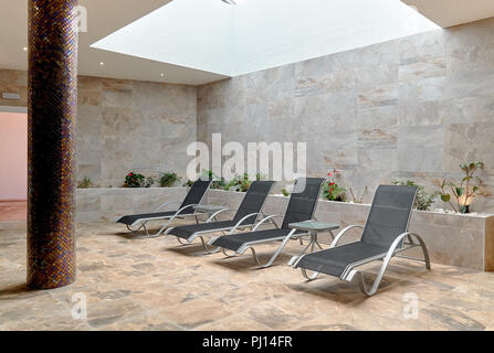 Vuoto grigio quattro sedie a sdraio all'interno della stanza piastrellata. Nessuno in sala spa. Sedia a sdraio per clienti relax dopo procedure termali Foto Stock