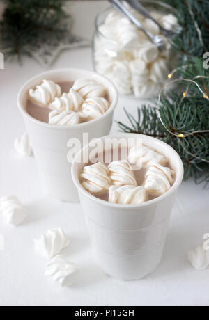 Il cacao con marshmelow in bianco tazze e marshmallows in un vasetto di vetro su un tavolo bianco con rami di abete rosso, una ghirlanda di fiori e una stella bianca. Messa a fuoco selettiva Foto Stock
