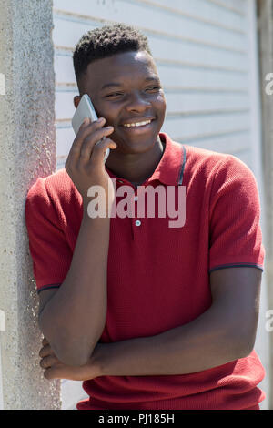 Ragazzo adolescente parlando al di fuori sul telefono cellulare in contesto urbano Foto Stock