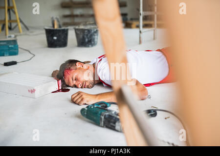 Un inconscio uomo lavoratore sdraiato sul pavimento dopo una lesione alla testa. Foto Stock