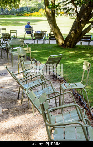 Un uomo solo lettura, seduti all'ombra su un prato di metallo sedia nel giardino del Lussemburgo a Parigi, Francia, con sedi sparse lungo i vicoli. Foto Stock