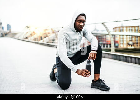 Giovane sportivo da uomo nero runner con una bottiglia d'acqua sul ponte in una città di riposo. Foto Stock