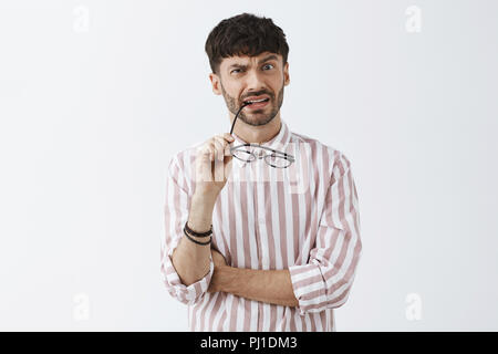 Vita-up shot di interrogato e confuso intensa ragazzo attraente con la barba di mordere di RIM di bicchieri accigliata e rendendo clueless espressione avendo problemi nel capire qualcosa di disagio Foto Stock