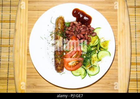 Su una piastra bianca con una opzione di servizio si trova un delizioso pasto. Le spezie vengono cosparsi con cetrioli freschi, fagioli rossi, pomodori, aneto e fritti in una skil Foto Stock