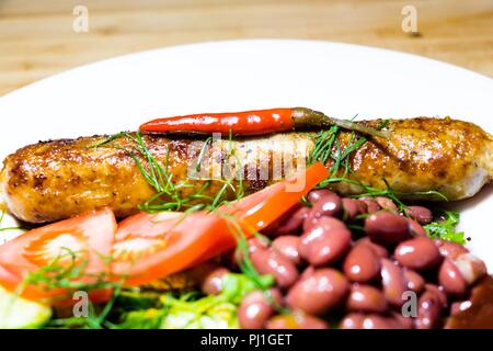 Su una piastra bianca con una opzione di servizio si trova un delizioso pasto. Le spezie vengono cosparsi con cetrioli freschi, fagioli rossi, pomodori, aneto e fritti in una skil Foto Stock