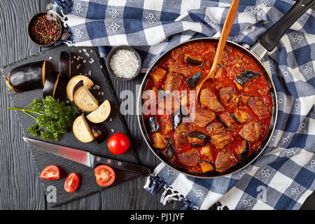 Khoresh Bademjan - melanzana stufato di manzo in una padella nera su di un tavolo di legno con ingredienti sul tagliere, propone cucina persiana, vista da sopra Foto Stock