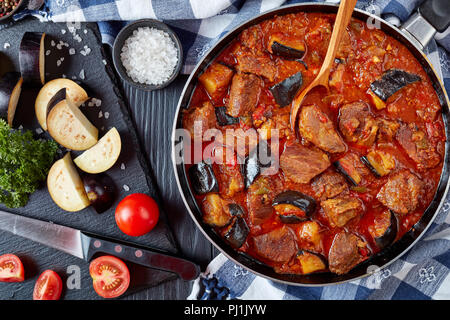 Aubergine stufato di manzo - Khoresh Bademjan in una padella su tavoli in legno nero con ingredienti su un tagliere, propone cucina persiana, vista da sopra, clo Foto Stock