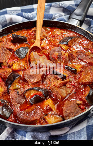 Close-up di melanzane spezzatino di manzo - Khoresh Bademjan in una padella su tavoli in legno nero, propone cucina persiana, verticale vista da sopra Foto Stock