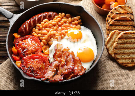 Prima colazione inglese con salsicce, pomodori grigliati, uova, bacon e fagioli in padella. Foto Stock