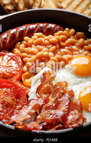 Prima colazione inglese con salsicce, pomodori grigliati, uova, bacon e fagioli in padella. Foto Stock