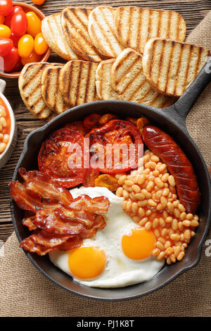 Prima colazione inglese con salsicce, pomodori grigliati, uova, bacon e fagioli in padella. Foto Stock