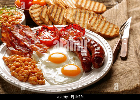 Prima colazione inglese con salsicce, pomodori grigliati, uova, pancetta, fagioli e pane sulla piastra bianca Foto Stock