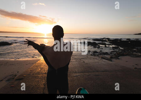 Surfer indossando il costume sulla spiaggia durante il tramonto Foto Stock