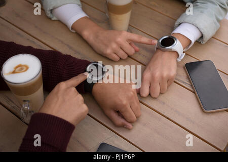 Paio utilizzando smartwatch in outdoor cafe Foto Stock