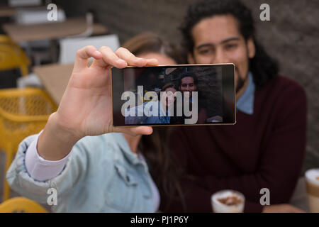 Giovane tenendo selfie a outdoor cafe Foto Stock