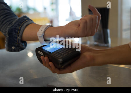 Donna pagando con la tecnologia NFC su smartwatch in cafe Foto Stock