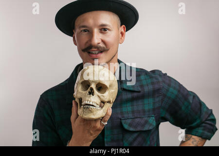 Uomo carino con tatuaggi tenendo un cranio il disegno su di esso tattoo Foto Stock