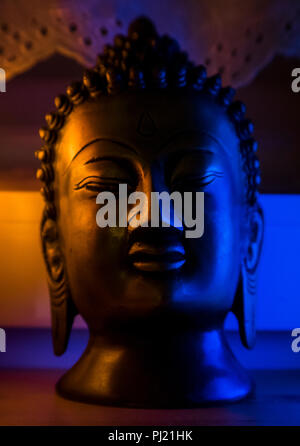 Busto nero scultura Buddha illuminato in blu e arancione Foto Stock