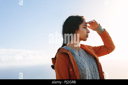 Ritratto di giovane donna in piedi all'aperto e guardando lontano con la mano sulla fronte. Femmina in un abbigliamento caldo fissando una vista. Foto Stock