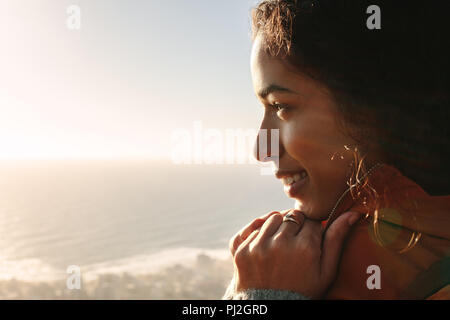 Close up volto sorridente della giovane donna africana che indossa una giacca calda guardando una vista all'esterno. Foto Stock